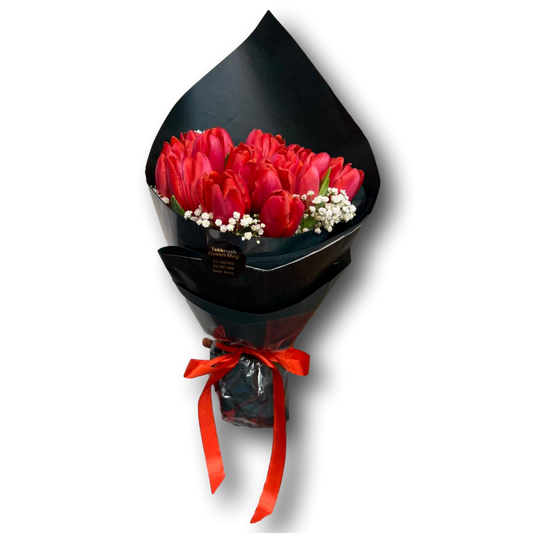 Bouquet of red tulips wrapped in black paper with a red ribbon on a white background