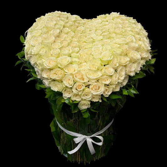 Heart-shaped arrangement of white roses on a dark surface with a colorful background.