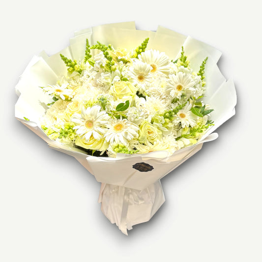 Full round bouquet of white gerbera daisies, cream roses, green snapdragons and white chrysanthemums, wrapped in white paper