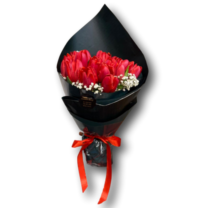 Bouquet of red tulips wrapped in black paper with a red ribbon on a white background